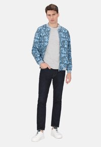 Giubbotto bomber blu con motivo floreale, t-shirt grigia, jeans scuri e sneakers bianche. Il giubbotto presenta polsini e colletto a costine.