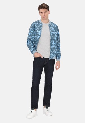 Blauwe bomberjack met bloemenpatroon, grijze t-shirt, donkere jeans en witte sneakers. Jack heeft ribgebreide manchetten en kraag.