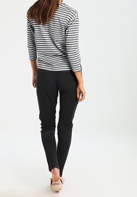 Striped black and white long-sleeve top with gray leggings. Both garments are fitted. The top features a round neckline and three-quarter sleeves.