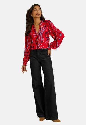 Red blouse with an abstract pattern in purple and black, featuring a V-neck and long, puffed sleeves. Paired with high-waisted black jeans.