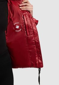 Sarkana polsterēta jaka ar spīdīgu virsmu, kas aprīkota ar iekšējo kabatu, Khujo logotipu un regulējamu siksnu pie apakšmala.