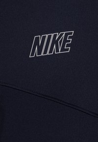 Námořnická modrá mikina Nike se zdůrazněným bílým logem, vyrobená z texturované látky se šitými akcenty. Design zahrnuje různorodé panely.