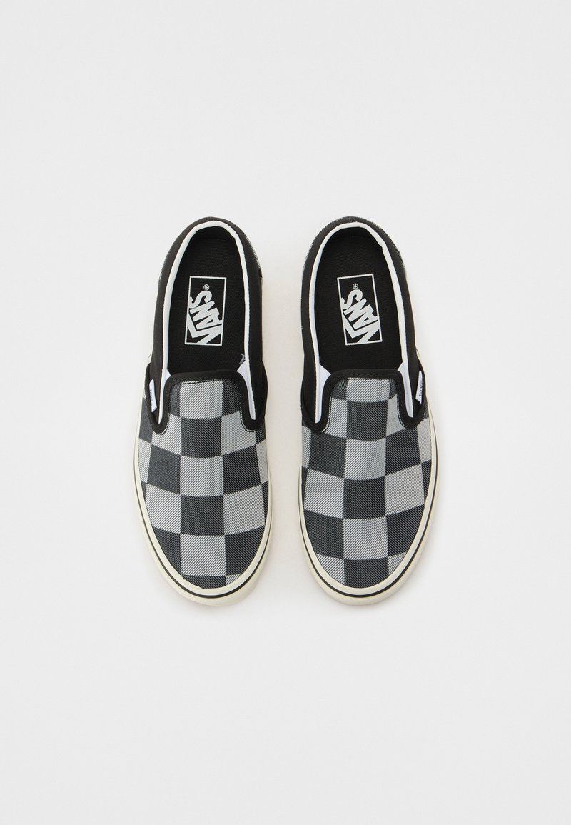 Zapatillas tipo slip-on en cuadros negros y grises con parte superior de lona, cuello acolchado y suelas de goma blanca, que presentan un logotipo en la lengüeta.