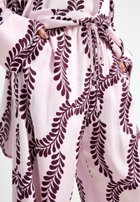 Set da lounge morbido di colore rosa con un motivo a foglie in viola scuro. Il tessuto ha una lucentezza simile alla seta, con una vestibilità comoda e un laccetto regolabile in vita.