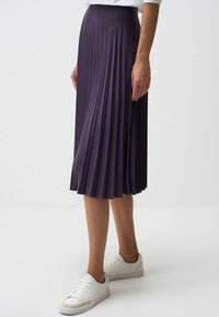 Gonna midi plissettata viola in tessuto leggero con vita elasticizzata. Indossata con sneakers bianche.