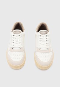 Baskets blanches et beiges avec une finition en cuir lisse, un bout perforé et des accents en daim doux. Comprend des lacets plats et une semelle en caoutchouc.