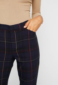 Pantalons à carreaux navy avec des accents rouges et dorés. Comprend une taille ajustée, une poche latérale et une texture de tissu lisse.