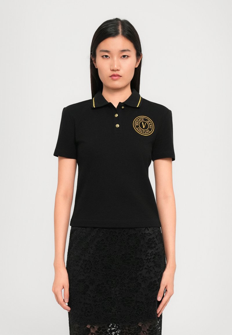 Black polo shirt with yellow accents, short sleeves, and a round embroidered logo on the chest. Smooth fabric with a fitted silhouette.