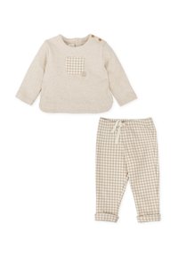 Top beige de manga larga con un bolsillo parche a cuadros y dos botones en el hombro, combinado con pantalones beige a cuadros con cintura ajustable.