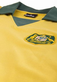 Geel poloshirt met een groene kraag, voorzien van een geborduurd Australisch wapen in het midden. Gladde stof met een V-hals ontwerp.