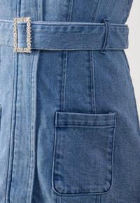 Heledast sinine denimkleit, millel on struktureeritud pind. Omab laia vööd, millel on ehted ja kaks esi-taskut.