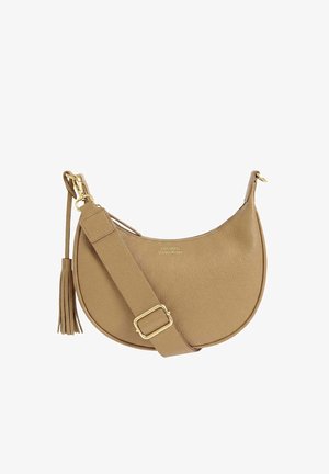 Sac à bandoulière en cuir couleur beige en forme de croissant, avec une large bandoulière ajustable, une boucle dorée, un détail pompon et un petit logo de la marque à l'avant.