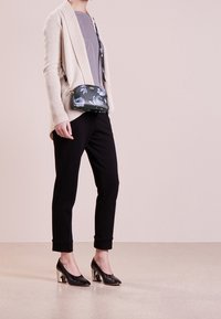 Beige pletený cardigan, šedý top, černé zúžené kalhoty, černé vysoké podpatky s průhledným podpatkem a kabelka přes rameno s květinovým vzorem.