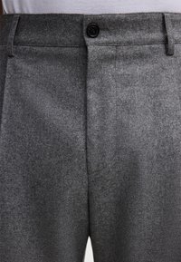 Szare wełniane spodnie z teksturowanym wykończeniem, z czarnym zapięciem na guzik i przednimi kieszeniami. Materiał wydaje się miękki i ciepły.