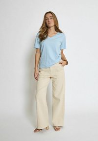 T-shirt azzurro chiaro a scollo a V abbinato a pantaloni beige a gamba larga. La t-shirt ha maniche corte e i pantaloni presentano tasche frontali e una texture liscia.