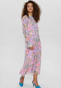 Robe florale en tissu léger et transparent rose, avec des motifs verts et orange. Manches longues, poignets boutonnés et longueur jusqu'aux chevilles.