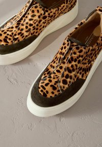 Leopard print slip-on shoes feature a suede trim, chunky white sole, and intricate texture on the fabric.