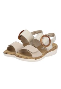 Sandali beige con due cinturini, uno con texture e uno liscio. Presenta un grande accento circolare marrone e una suola in sughero imbottita.