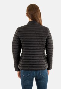 Giubbotto piumino nero con dettagli trapuntati, colletto alto e design aderente. Indossato sopra jeans in denim, evidenziando una silhouette elegante.