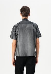 Short-sleeved shirt with a black and white plaid pattern, collared design, and a straight hem, made from a lightweight fabric.