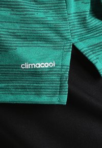 Zelené sportovní tričko z látky s texturovaným vzorem. Má rozparek na lemu a výrazné bílé logo "climacool".