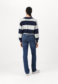 Pull rayé bleu marine et gris avec des poignets côtelés, associé à un jean évasé bleu foncé avec des coutures détaillées et une étiquette noire à la taille.