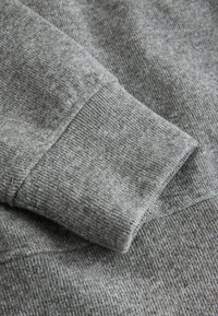 Poignet de sweat-shirt gris à texture côtelée, avec un tissu doux et mélangé, et un design classique à coupe droite.