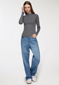 Szary, długi rękaw z wysokim kołnierzem, połączony z luźnymi niebieskimi dżinsami i białymi sneakersami. Gładka tekstura i luźny krój.