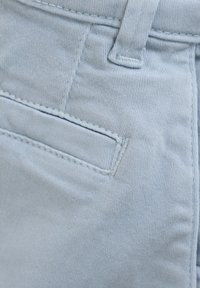 Ljusblå denimtyg med en sidficka med synliga sömmar och en slät textur. Tyget är mjukt med en subtil strech.