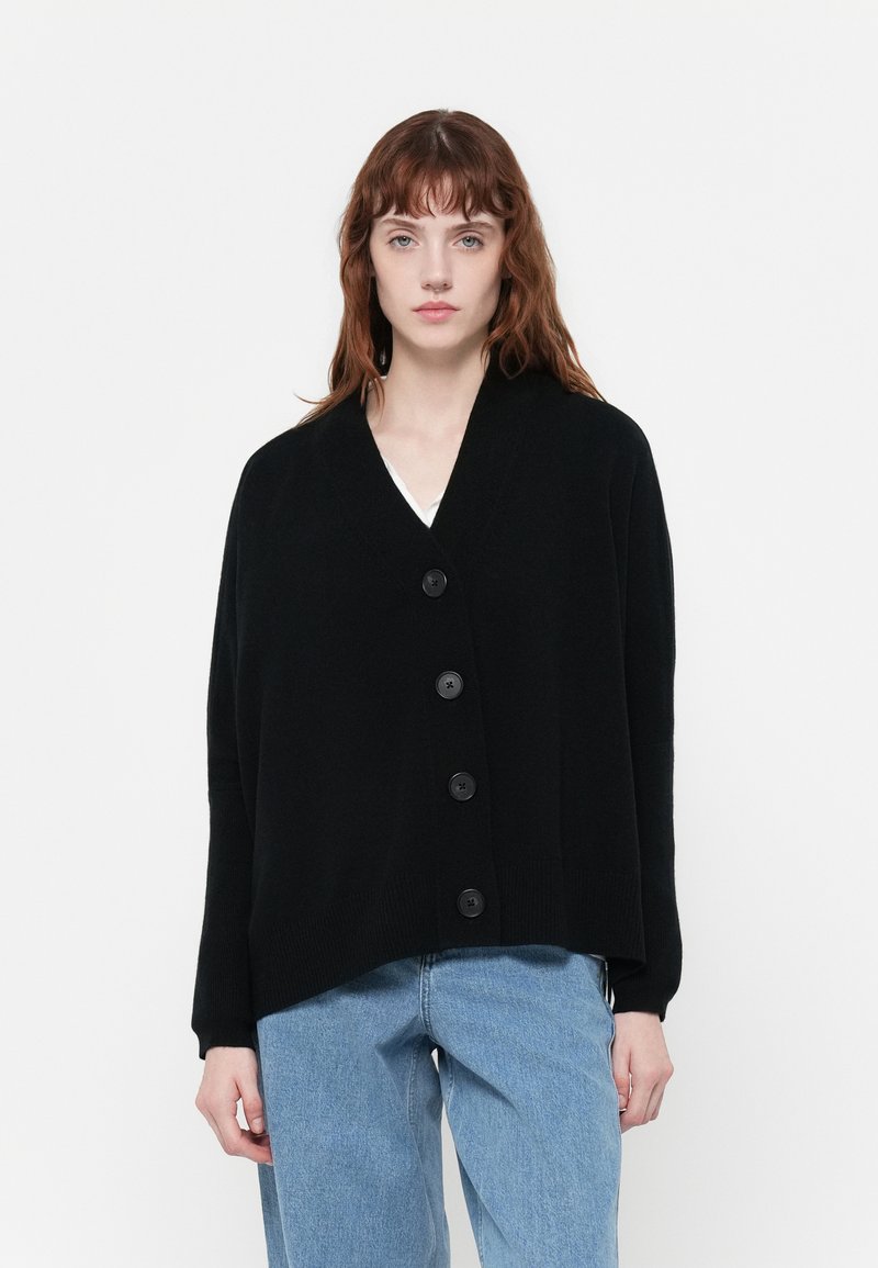 Čierny oversized cardigan vyrobený z mäkkej pleteniny, s výstrihom do V, dlhými rukávmi a piatimi veľkými gombíkmi na prednej strane.