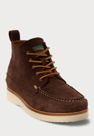 Brown suede ankle boot with a rounded toe, contrasting cream sole, brown laces, and decorative stitching along the edge.