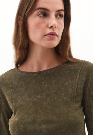 Maglietta verde oliva a maniche lunghe realizzata in tessuto morbido, con scollatura rotonda e una sottile texture sbiadita con dettagli di cucitura visibili.