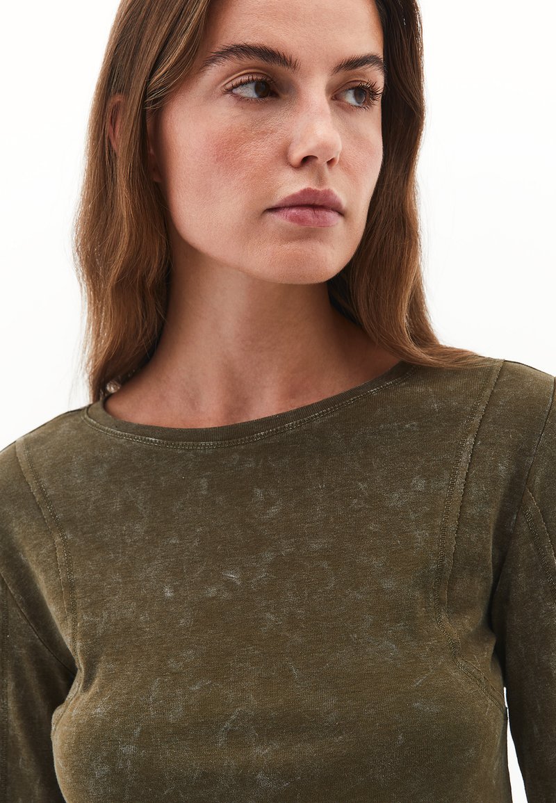 Top de manga larga verde oliva hecho de una tela suave, con cuello redondo y una sutil textura desteñida con detalles de costura visibles.