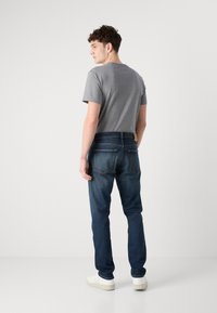 Tmavomodré jeans s úzkym strihom, v kombinácii so sivým bavlneným tričkom. Vlastnosti zahŕňajú zadné vrecká a koženú nášivku na páse.