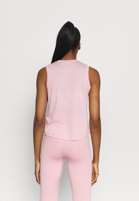 Haut sans manches rose pâle avec un col rond, présentant une coupe semi-ample et des coutures contrastantes le long des emmanchures.