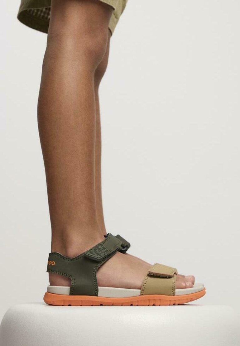 Sandales pour enfants avec une tige verte, des brides beiges et des semelles en caoutchouc orange ; dotées de brides réglables en Velcro et d'un design léger.