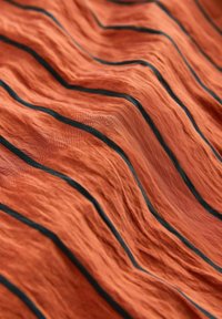 Tissu texturé en orange brûlé avec des motifs ondulés et des rayures bleu foncé. Surface lisse avec des dimensions plissées, créant profondeur et intérêt.