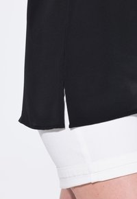 Blusa nera a maniche corte con orlo curvo e spacco laterale, abbinata a pantaloni shorts in denim bianco con orlo piegato. Tessuto dalla texture liscia.