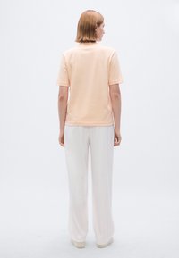 Ροδακινί κοντομάνικη μπλούζα με στρογγυλή λαιμόκοψη, συνδυασμένη με λευκό παντελόνι φαρδιάς γραμμής. Το σύνολο έχει απαλή υφή και χαλαρή εφαρμογή.