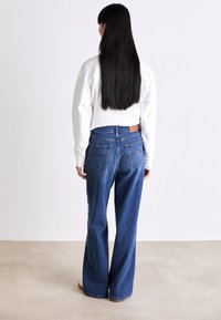 Jeans de mezclilla azul de cintura alta con un ajuste relajado, piernas amplias y bolsillos traseros. Acompañados de una blusa blanca de manga larga.