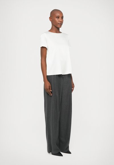 Λευκό κοντομάνικο μπλουζάκι με στρογγυλή λαιμόκοψη, συνδυασμένο με γκρίζες παντελόνες τύπου wide-leg. Μαλακό ύφασμα και άνετη εφαρμογή. Μαύρα μυτερά παπούτσια ολοκληρώνουν την εμφάνιση.