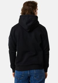 Felpa nera con grande cappuccio, vestibilità comoda e polsini a coste. Presenta una tasca applicata sul maniche sinistra, realizzata in morbido tessuto testurizzato.