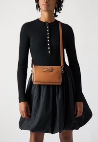Brown leather crossbody bag with a textured finish, silver hardware, and contrasting white stitching. Features a stylish clasp and adjustable strap.