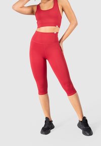 Top corto atletico rosso e leggings capri realizzati in tessuto elasticizzato, caratterizzati da un design aderente e cuciture piatte. Abbinati a sneakers nere.
