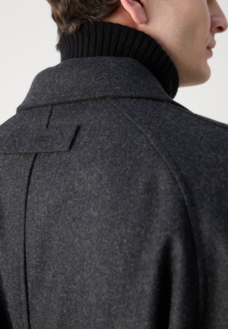 Manteau en laine gris foncé avec un col montant noir à côtes, présentant une couture au dos et des détails couturés subtils.