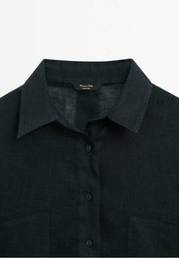 Chemise noire à boutons avec col pointu et poches poitrine en tissu texturé.