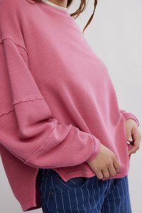 Ροζ ριμπ μακρυμάνικη μπλούζα με άνετη εφαρμογή, με ακατέργαστες άκρες και χαλαρούς ώμους, συνδυασμένη με μπλε παντελόνι με λεπτές ρίγες.