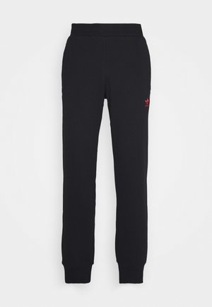 Sorte Adidas træningsbukser med elastisk talje og manchetter, med et lille rødt Adidas-logo på den øverste venstre lår.