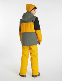 Giacca invernale colorata con una parte superiore grigia, una parte centrale gialla e maniche nere. Abbinata a pantaloni gialli vivaci e a un berretto coordinato.
