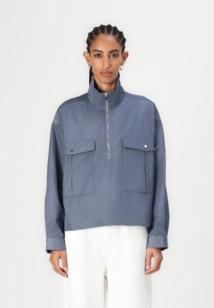 Blue, zip-up jacket with a high collar, two front patch pockets, and loose fit. Smooth fabric with subtle sheen, long sleeves, and minimal detailing.